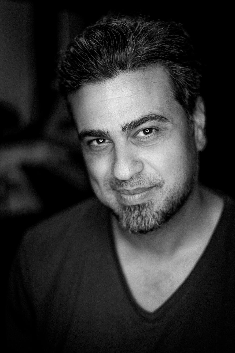 Black-and-white portrait of Arash Afshar looking confidently into camera, set against a soft background — direct, grounded, and trustworthy.